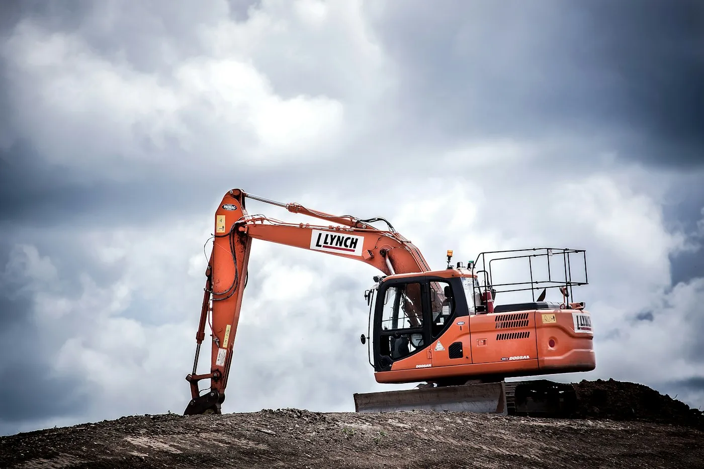 Excavator on a mound beneath a cloudy sky